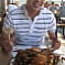 A person in a striped shirt, possibly William L., is seated at a table, smiling and holding utensils, with a large plate of cooked seafood in front of them. Other diners are visible in the background.