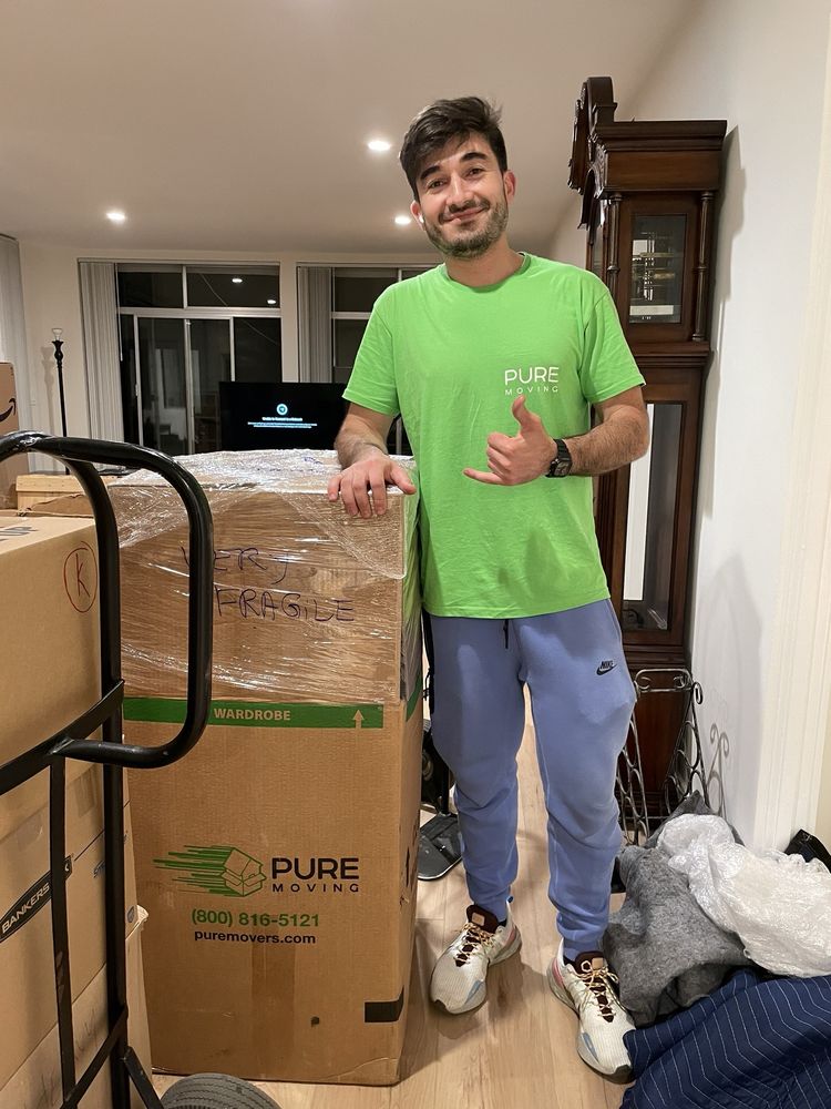 Pure Movers employee standing beside wrapped fragile moving boxes indoors