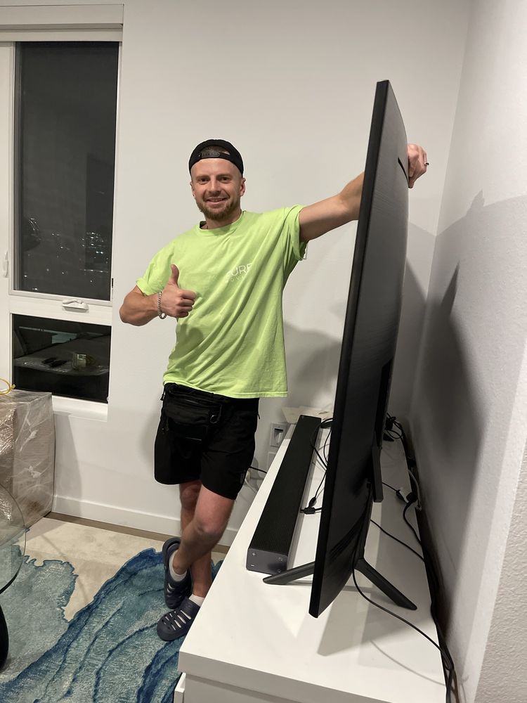 Pure Movers employee standing beside large television after delivery setup
