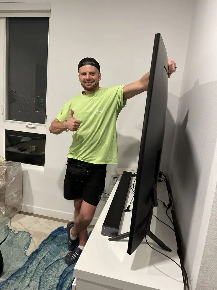 Pure Movers employee standing beside large television after delivery setup