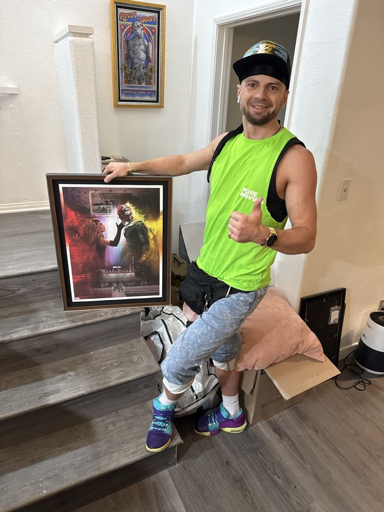 Friendly mover holding framed artwork near staircase during residential move