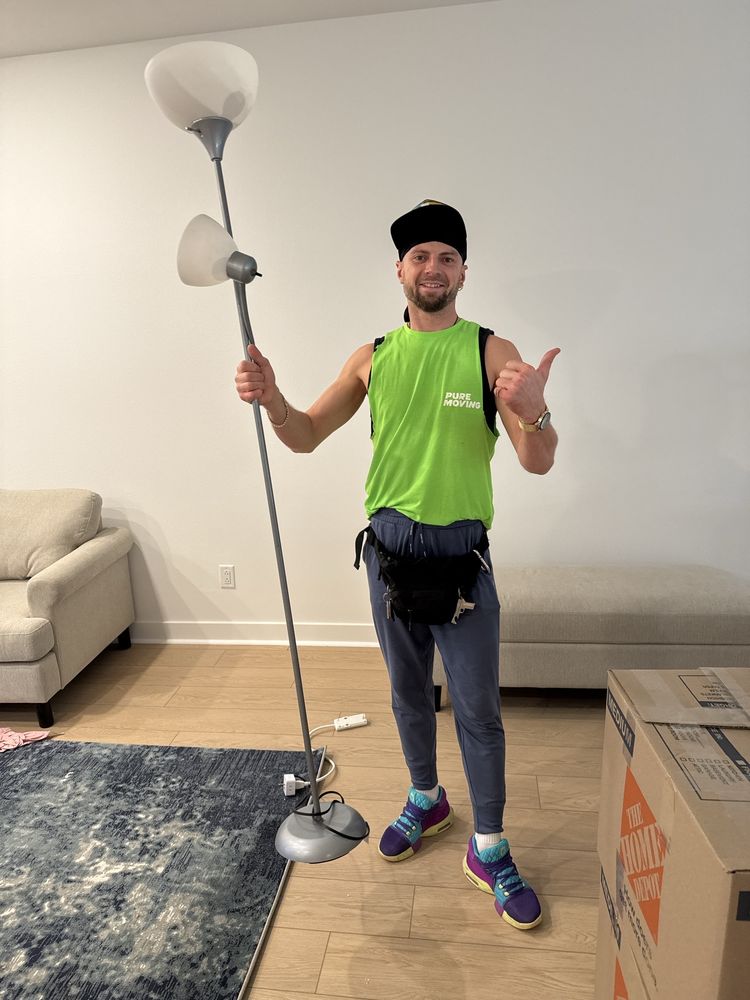 Professional mover holding floor lamp inside furnished apartment during move-in service