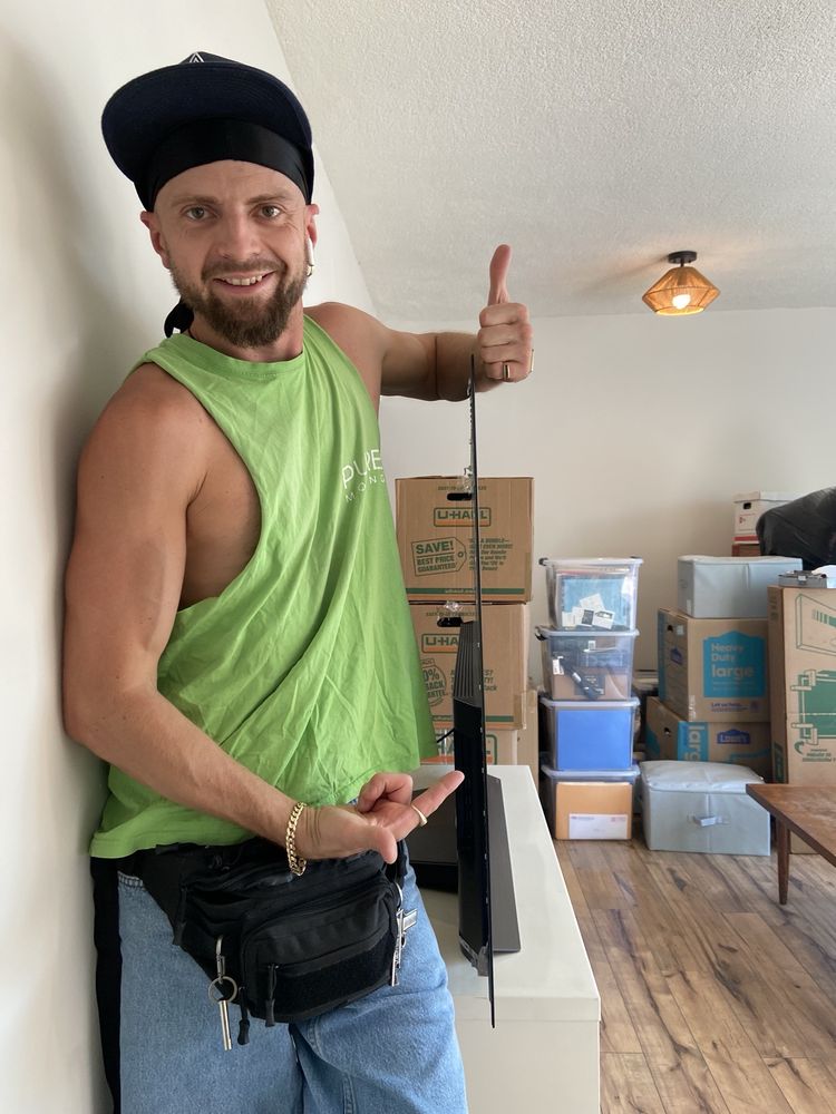 Friendly mover standing beside mounted television and packed moving boxes in apartment