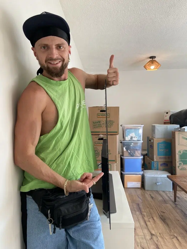Friendly mover standing beside mounted television and packed moving boxes in apartment