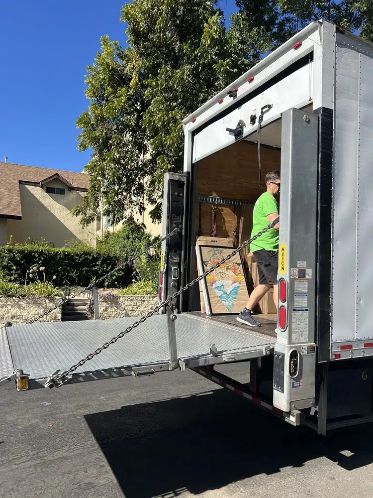 Professional mover loading furniture into a moving truck with liftgate in residential neighborhood