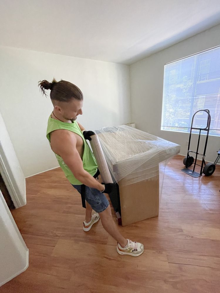 Mover carrying wrapped furniture through empty apartment during residential move